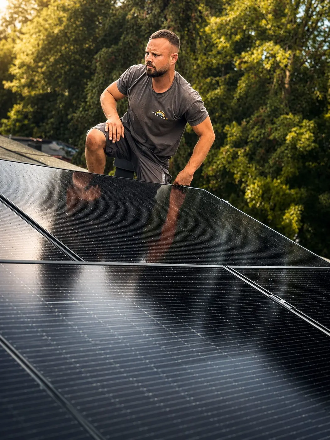 Modulmontage auf einem Schrägdach durch SolarX Monteur kniet bei der Modulmontage auf einem Schrägdach zwischen schwarzen Solarmodulen