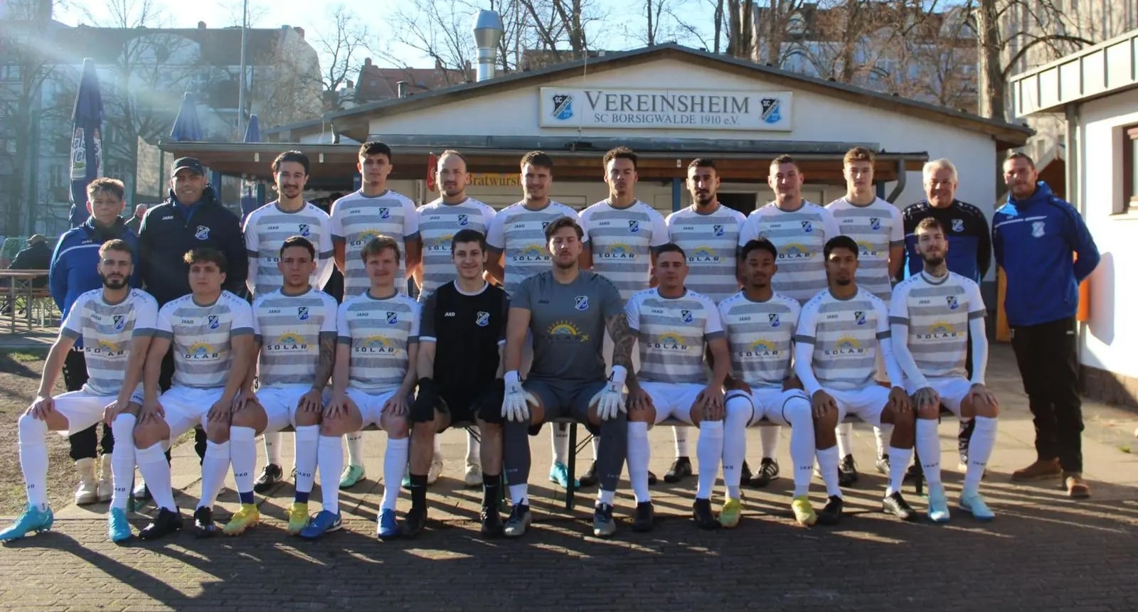 Mannschaft des SC Borsigwalde mit SolarX als Sponsor Unser Team des SC Borsigwalde 1910 in zwei Reihen vor dem Vereinsheim des Vereins, auf der Brust der grau-weiß gestreiften Trikots das Logo der SolarX GmbH