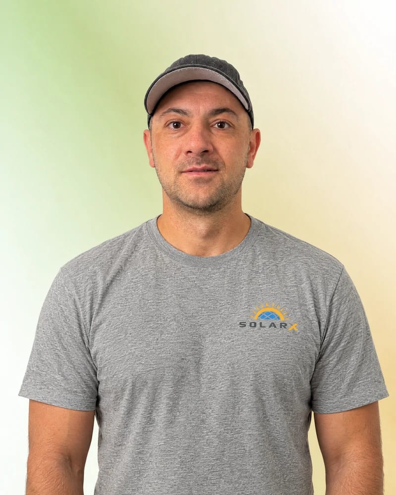 Dimitri – DC-Monteur von SolarX Dimitri mit schwarzer Cap und grauem SolarX-Teamshirt vor dem grün-goldenen Porträthintergrund.